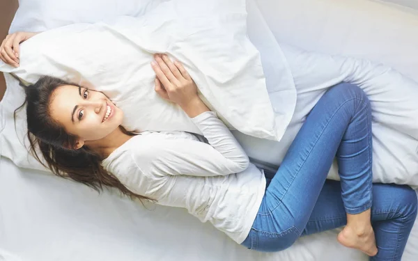 Młoda kobieta, leżąc na łóżku, przytulanie poduszkę — Zdjęcie stockowe