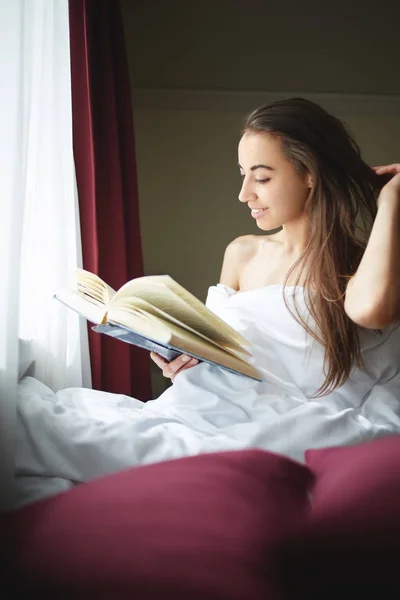 Uma mulher senta-se perto de uma janela com um livro velho — Fotografia de Stock