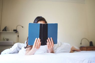 yatakta yatarken kitap ile genç bir kadın