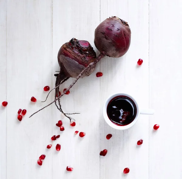 Beet, pomegranate seeds and Cup with beet juice on white wooden table — Stock Photo, Image