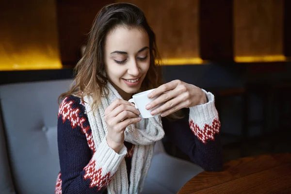 Mujer sonriente vestida con un suéter y bufanda en la cafetería con taza de café — Foto de Stock