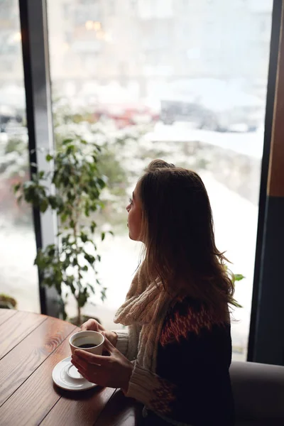 Hymyilevä nainen pukeutunut villapaita ja huivi kahvilassa kupin kahvia — kuvapankkivalokuva
