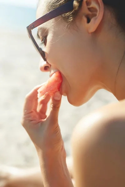 Nuori kaunis nainen syö vesimelonia rannalla — kuvapankkivalokuva