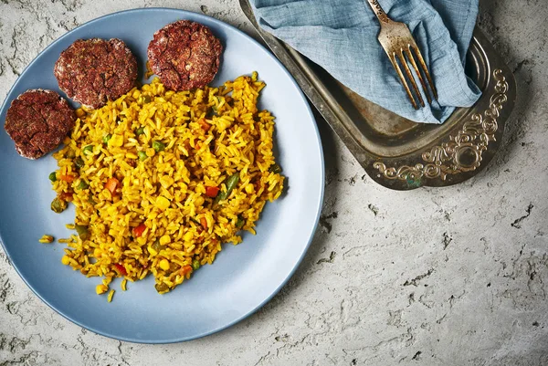 Vista superior de um risoto com legumes e costeletas de beterraba vegan servidos em um prato azul em um fundo de concreto cinza — Fotografia de Stock