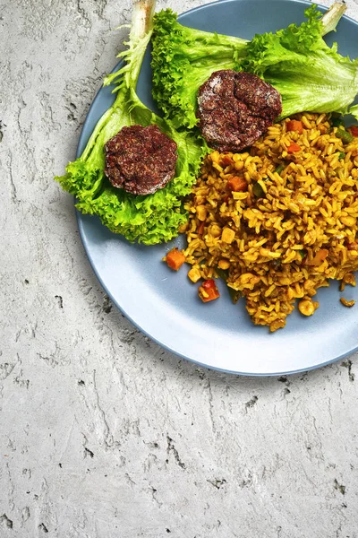 Vista superior de um risoto com legumes e costeletas de beterraba vegan servidos em um prato azul em um fundo de concreto cinza — Fotografia de Stock