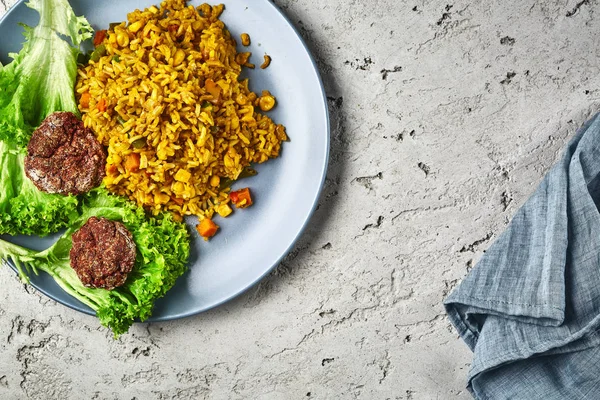 Vista superior de um risoto com legumes e costeletas de beterraba vegan servidos em um prato azul em um fundo de concreto cinza — Fotografia de Stock