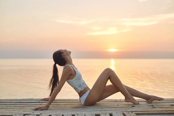 Piękna kobieta seksualne w biały kapelusz i bikini na drewnianym molo morze i zachód słońca — Zdjęcie stockowe