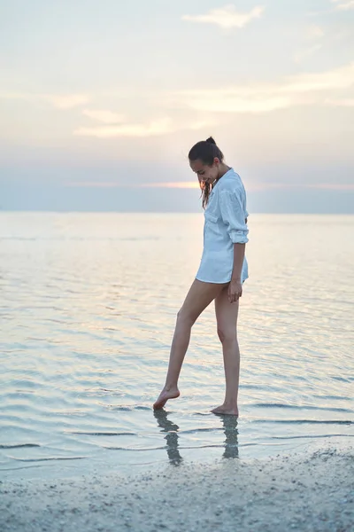 Hermosa mujer sexual en camisa blanca y bikini caminando en la playa contra el mar y la puesta de sol — Foto de Stock