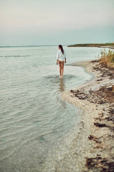 Hermosa mujer sexual en camisa blanca y bikini caminando en la playa contra el mar y la puesta de sol — Foto de Stock