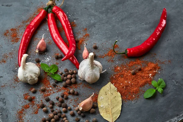 Food cooking background with chili peppers, garlic and spices on dark stone table. — Stock Photo, Image