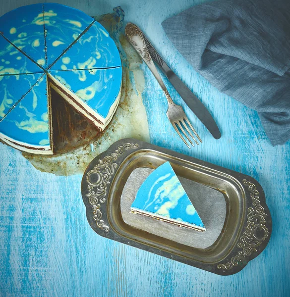 Gesneden koek en stuk van mousse taart met blauwe glaze op een zoek zoals zilver, vintage metalen schotel op de houten achtergrond wit-blauw — Stockfoto