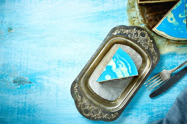 Gesneden koek en stuk van mousse taart met blauwe glaze op een zoek zoals zilver, vintage metalen schotel op de houten achtergrond wit-blauw — Stockfoto