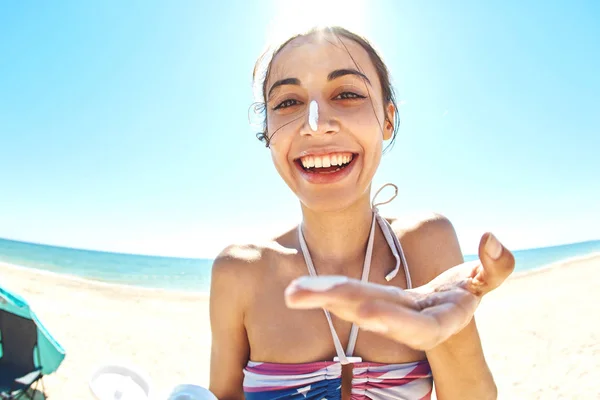 Houkutteleva hymyilevä nainen terveellä iholla soveltamalla aurinkovoidetta aurinkoisella rannalla — kuvapankkivalokuva