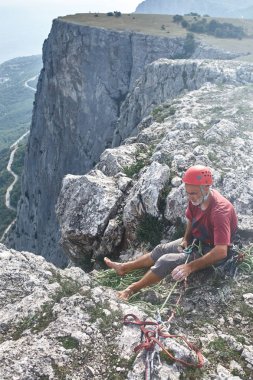 adam kaya tırmanışçısı uçurum üstüne oturur ve bir ortak belays