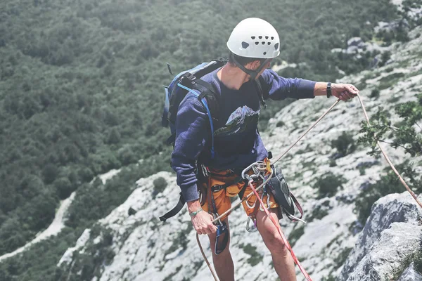 Homem escalador de rocha no topo do penhasco e atrasa um parceiro — Fotografia de Stock