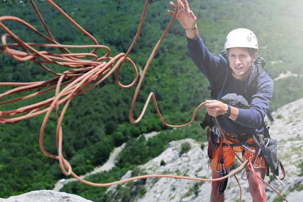 Man rock climber on the top of the cliff and throws a rope to a partner — Stock Photo, Image