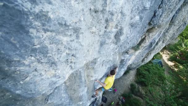 Vista superior del hombre escalador de roca en camiseta amarilla, sube a un acantilado, buscando, alcanzando y agarrando bodega. al aire libre escalada en roca y concepto de estilo de vida activo — Vídeo de stock
