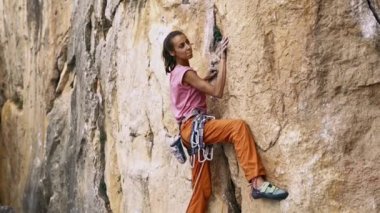 Genç bayan kaya tırmanışçısı bir uçuruma tırmanmaya çalışıyor. Arıyor, uzanıyor ve tutunuyor..