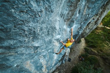 Sarı tişörtlü, kayalıklara tırmanan adamın en üst görüntüsü.