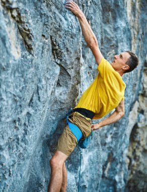 Genç ve güçlü bir adam yüksek bir kireçtaşı uçurumunda zorlu bir yola tırmanıyor..