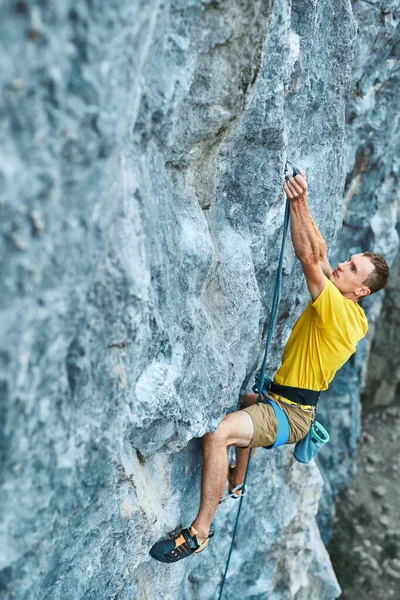 Молодой сильный мужчина скалолаз в желтой футболке, взбирающийся на скалу — стоковое фото