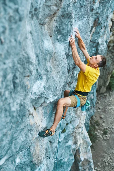 Junger kräftiger Mann, Bergsteiger in gelbem T-Shirt, klettert an einer Klippe — Stockfoto