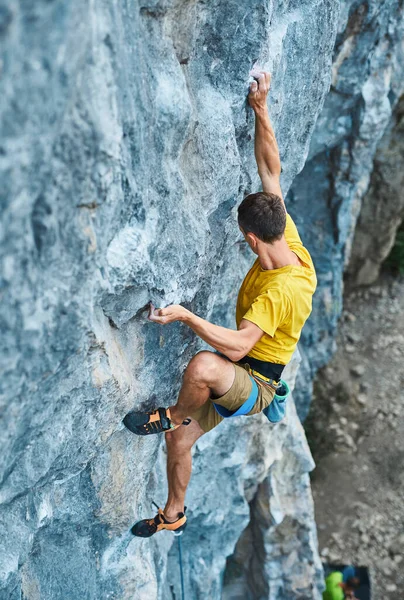 Young strong man rock climber in yellow t-shirt, climbing on a cliff — Stock Photo, Image