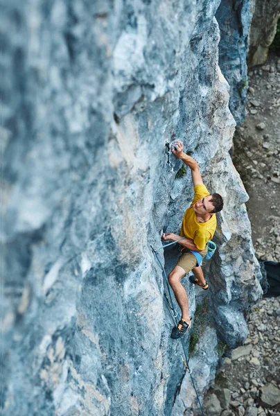Vista superior del hombre escalador de roca en camiseta amarilla, sube a un acantilado, buscando, alcanzando y agarrando bodega. al aire libre escalada en roca y concepto de estilo de vida activo —  Fotos de Stock