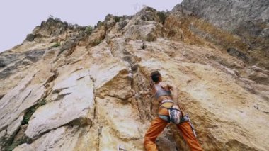 Genç fit kadın kaya tırmanışçısı dağa tırmanıyor, arıyor, uzanıyor ve sıkıca tutuyor.