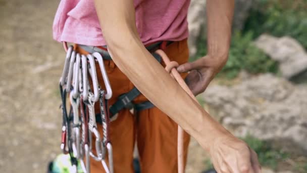 Detalle de escalada en roca del arnés de escalador con engranaje y manos agarrando la cuerda y haciendo nudo ocho — Vídeos de Stock
