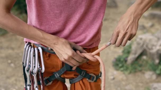 Detalle de escalada en roca del arnés de escalador con engranaje y manos agarrando la cuerda y haciendo nudo ocho — Vídeo de stock