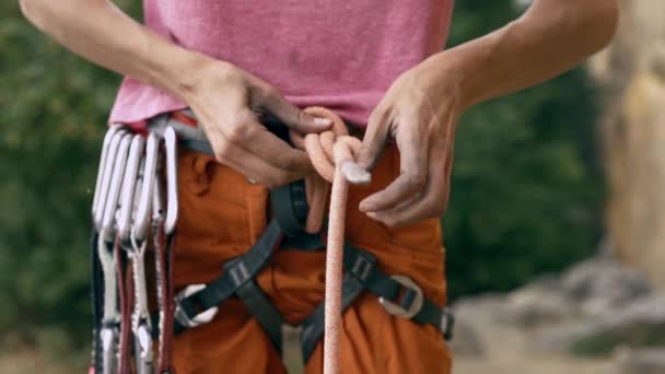 Detalle de escalada en roca del arnés de escalador con engranaje y manos agarrando la cuerda y haciendo nudo ocho — Vídeo de stock