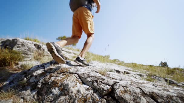 Wide angle slow motion feet young adult man hiker walking up the rocky slope at summer day against blue sky — Stock Video