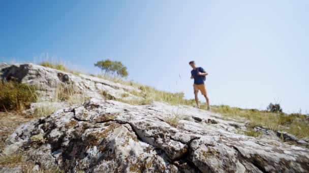 Groothoek slow motion voeten jonge volwassen man wandelaar lopen langs de rotsachtige helling in de zomer dag tegen de blauwe lucht — Stockvideo