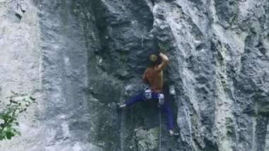 Arkaya bakan güçlü kaslı adam kaya tırmanışçısı dikey bir uçurumda spor rotasına tırmanıyor.