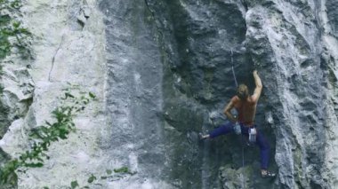 Arkaya bakan güçlü kaslı adam kaya tırmanışçısı dikey bir uçurumda spor rotasına tırmanıyor.