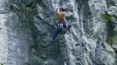 Arkaya bakan güçlü kaslı adam kaya tırmanışçısı dikey bir uçurumda spor rotasına tırmanıyor.