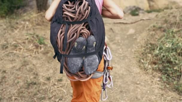 Detalles de escalada en roca. mujer vista trasera con mochila para equipos de escalada caminando al acantilado . — Vídeos de Stock