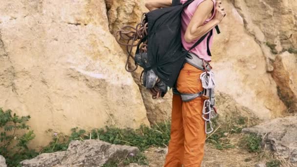 Détails de l'escalade. vue arrière femme avec sac à dos pour l'équipement d'escalade marchant vers la falaise et enlève son sac à dos et le pose sur le sol — Video