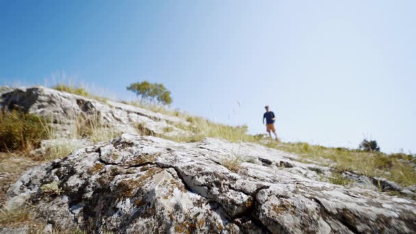 Geniş açı yavaş çekim ayak genç yetişkin yürüyüşçü yaz günü mavi gökyüzüne karşı kayalık yamaçta yürüyor — Stok video