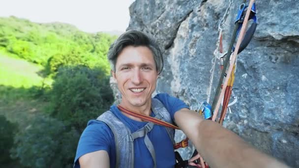 Man photographer capturing video selfie while hanging on climbing ropes on the cliff — Stock Video