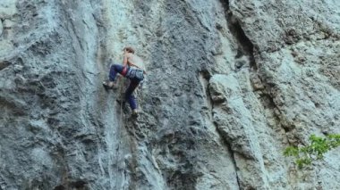 Arkaya bakan güçlü kaslı adam kaya tırmanışçısı dikey bir uçurumda spor rotasına tırmanıyor.