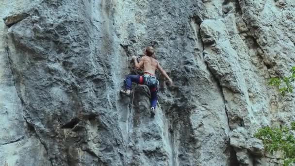 Arkaya bakan güçlü kaslı adam kaya tırmanışçısı dikey bir uçurumda spor rotasına tırmanıyor. — Stok video