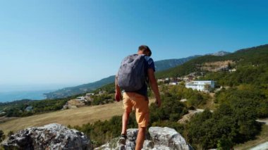 Mutlu bir yürüyüşçü uçurumun kenarında durur dağlarda, gökyüzünde ve denizde ve yükselen ellerde.