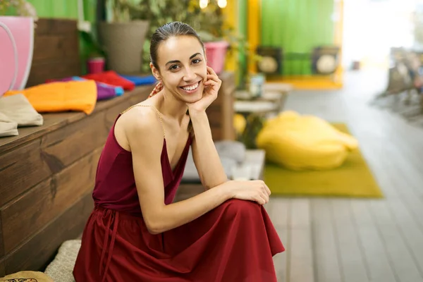 Young attractive woman in stylish red dress sitting on a sofa in a cafe with colorful background. — Stock Photo, Image