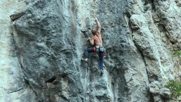 Homem forte muscular escalador de rocha escalada na rota do esporte ao ar livre em um penhasco vertical — Vídeo de Stock