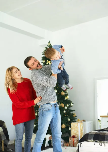 Jouluperhe viettää aikaa yhdessä kotona. Isä leikkii pienen poikansa kanssa joulukuusen lähellä kotona. . — kuvapankkivalokuva