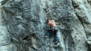 Arkaya bakan güçlü kaslı adam kaya tırmanışçısı dikey bir uçurumda spor rotasına tırmanıyor.