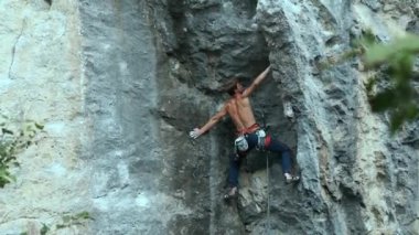 Arkaya bakan güçlü kaslı adam kaya tırmanışçısı dikey bir uçurumda spor rotasına tırmanıyor.