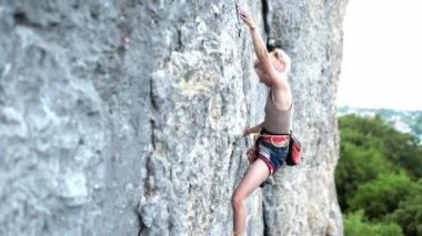 Siyah saçlı sporcu kadın dağlarda spor yaparken kayaya tırmanıyor..